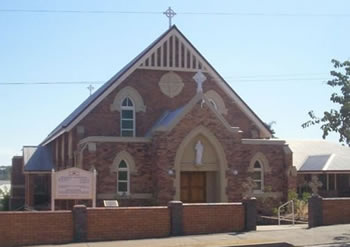 stone church-style school building with arched windows, cross roof feature, and brick fence at front entrance