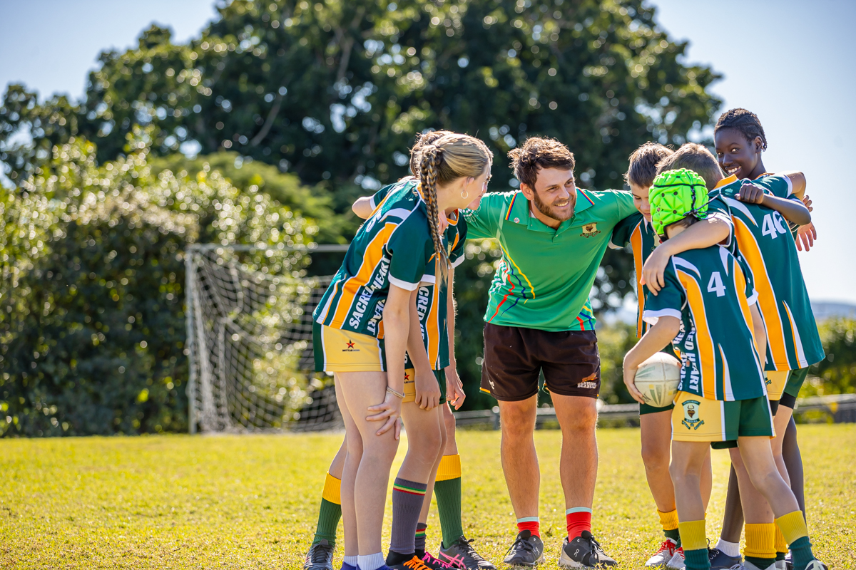 students in school sports uniforms huddled with coach on grassy field during outdoor training session