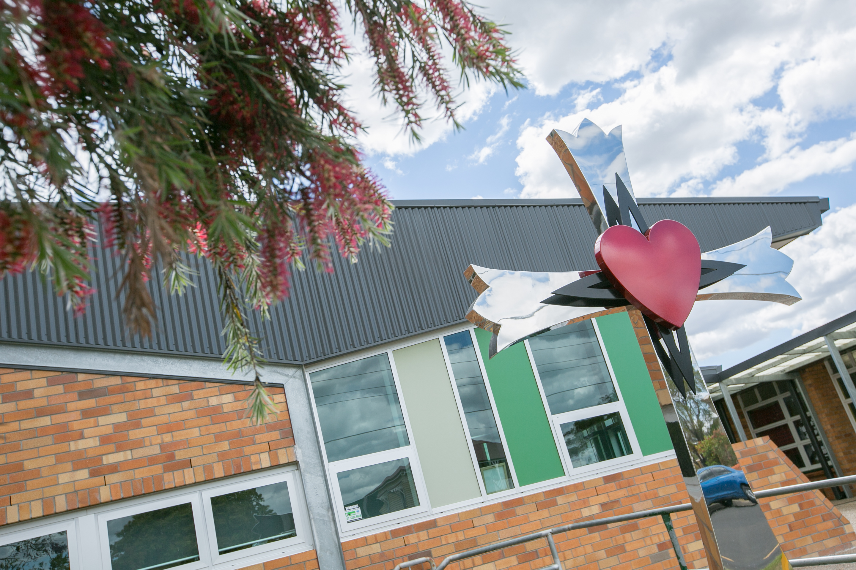 school building with modern brick facade and heart sculpture feature near entrance under flowering tree